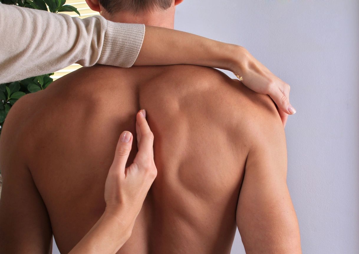 A person is holding their back while another person touches his shoulder.